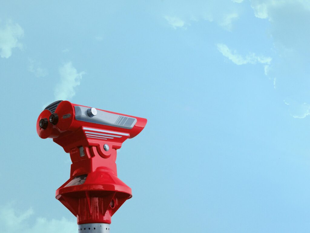 Red sightseeing telescope pointing against a bright blue sky, ideal for travel exploration concepts.