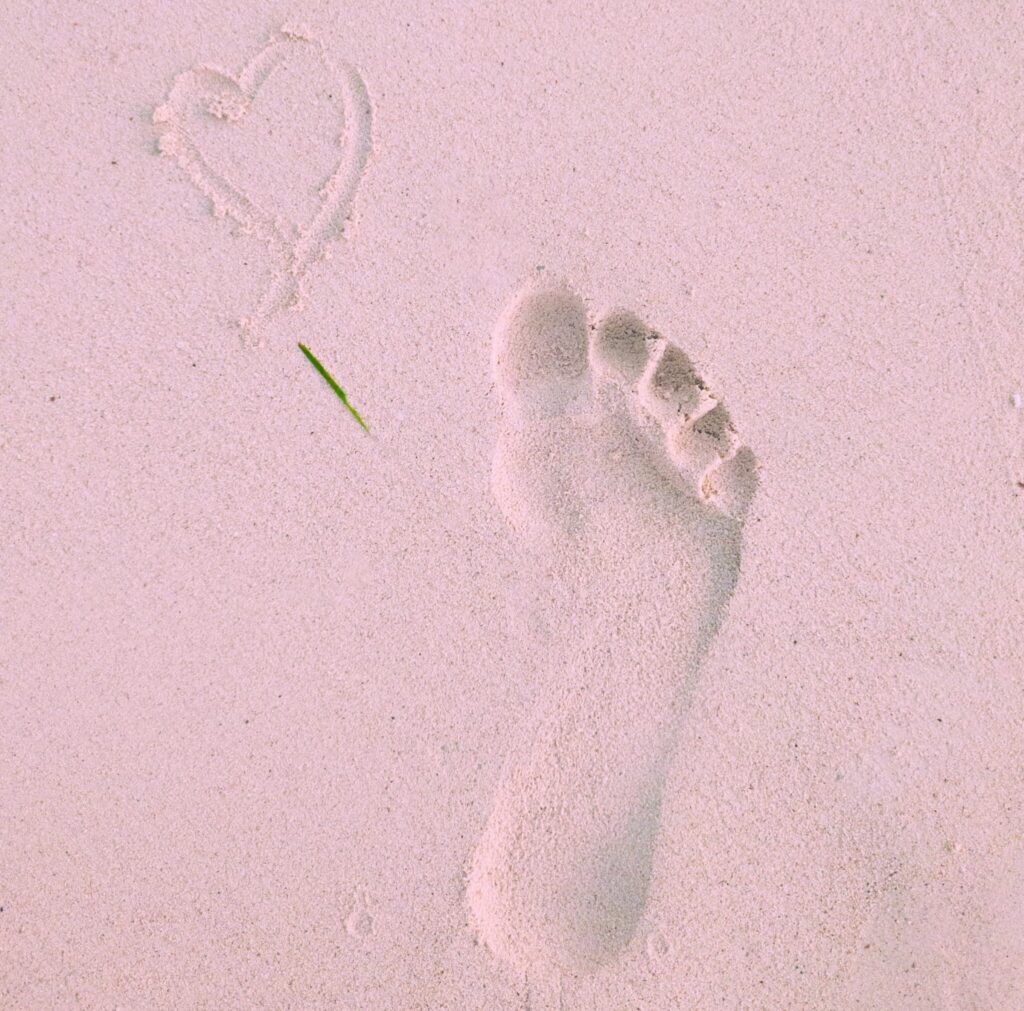 A footprint and heart drawn in sand at the beach, symbolizing love and travel.